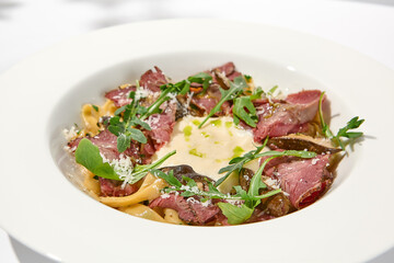 Homemade pasta with pastrami and creamy sauce with cheese. Italian pasta pappardelle with beef and sauce on white table Italian food in summer dining with shadows of sunlight