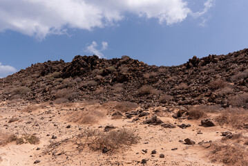 Dark black to brown volcanic elevations surrounded by light colored desert sands, Canary Islands