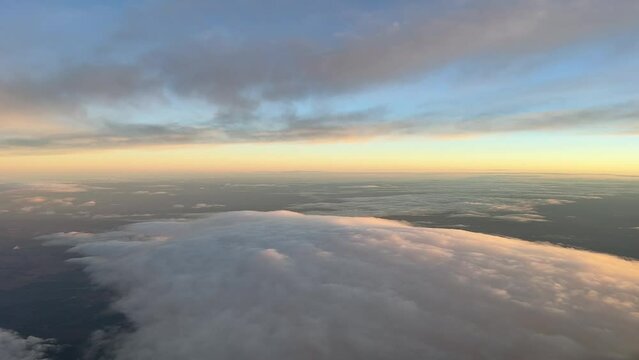 Pilot point of view while flying at dawn with an orange and blue sky over some clouds.