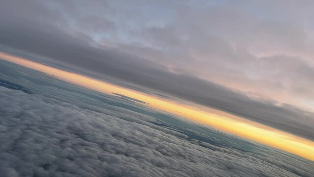 Pilot point of view from a jet cockpit during a left turn at dawn while flying between layers of clouds with an ogange sky.