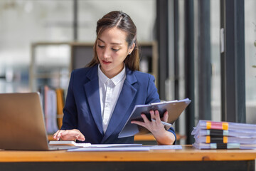 Brown haired wearing light blue jacket smiling Asian woman work with document laptop in office,...