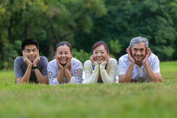 Portrait of group of Asian family with father, mother, son and daughter lying down together on the grass lawn at the public park during weekend activity for recreation and wellbeing concept
