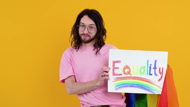 Young activist smiling happy fun gay man in pink t-shirt holding a protest sign during a LGBT pride parade isolated on yellow background studio. People lgbt lifestyle concept