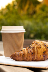 Fresh baked chocolate croissant on paper cup with lid for tea to go. Empty paper notebook....