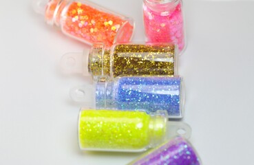Golden glitters in a small glass bottle with colorful glitters blur small bottles isolated on white background.