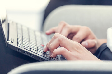 Young millennial woman typing on laptop. Closeup on hands. Day light dynamic workplace.
