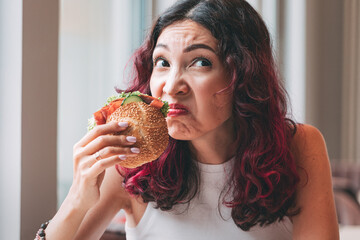 A girl sniffs a spoiled burger. Fast food diet and food poisoning concept - obrazy, fototapety, plakaty