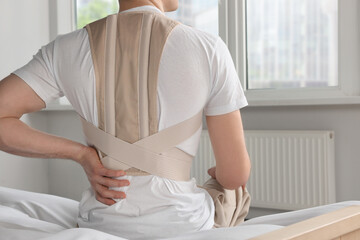 Closeup of man with orthopedic corset sitting in room, back view