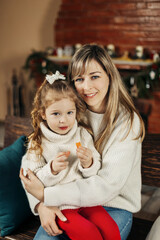 Beautiful mother and daughter on the background of a fireplace decorated for Christmas. Portrait of a loving family in close-up. Merry Christmas and Happy holidays