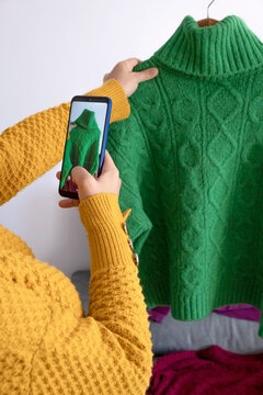 woman with phone in hand, taking photo of clothes to sell second-hand