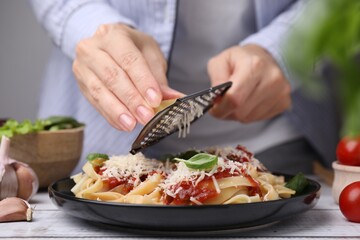 Woman grating parmesan cheese onto delicious pasta at wooden table, closeup