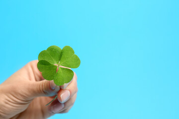 Woman holding beautiful green four leaf clover on light blue background, closeup. Space for text