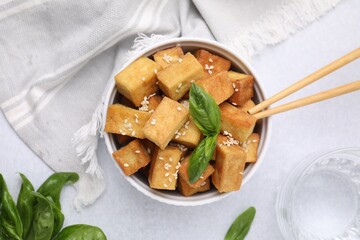 Bowl with delicious fried tofu, basil and sesame seeds on white table, flat lay