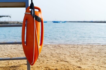 Fototapeta premium Sandy beach with an orange rescue buoy on an iron stand with the sea in the background, Egypt