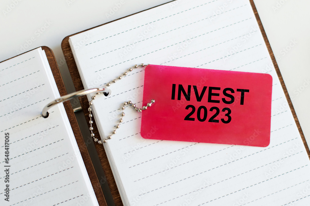 Poster invest 2023 text card on the background of an open notebook on the table
