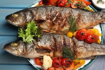 Plate with delicious roasted sea bass fish and vegetables on light blue table