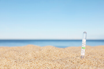 Weather thermometer in sand near sea, space for text