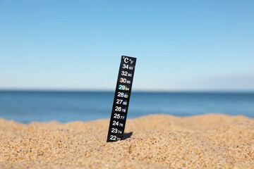 Black weather thermometer in sand near sea