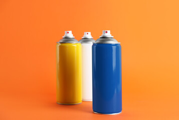 Colorful cans of spray paints on orange background
