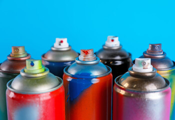 Used cans of spray paints on light blue background, closeup