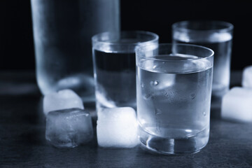 Shot glasses of vodka with ice on dark table, closeup