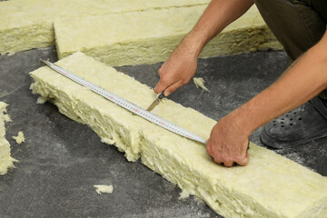 Worker measuring and cutting insulation material indoors, closeup