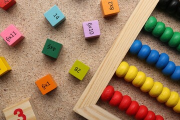 Wooden cubes with numbers and multiplications near abacus on fiberboard, flat lay