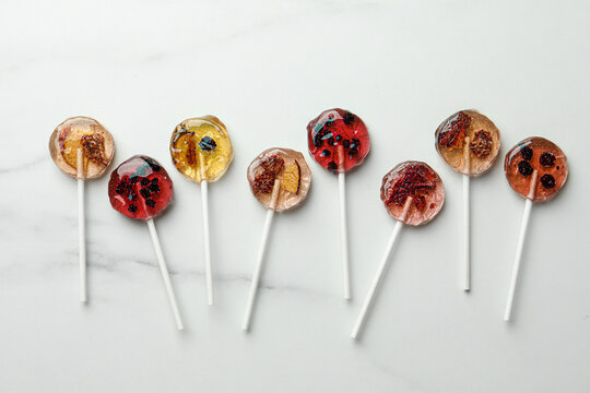 Sweet colorful lollipops with berries on white marble table, flat lay
