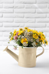 Beautiful bouquet of bright wildflowers in watering can on white wooden table near brick wall