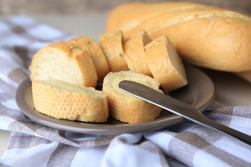 Whole and cut baguettes with fresh butter on checkered tablecloth, closeup