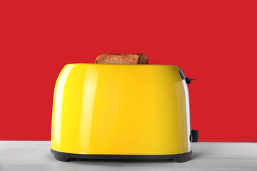Modern toaster with slices of roasted bread on white wooden table