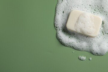 Soap and fluffy foam on green background, top view. Space for text