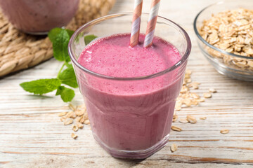 Glass of blackberry smoothie with straws, mint and oatmeal on light wooden table, closeup