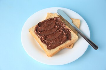 Tasty toast with chocolate paste on light blue background