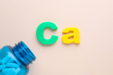 Open bottle and calcium symbol made of colorful letters on beige background, flat lay