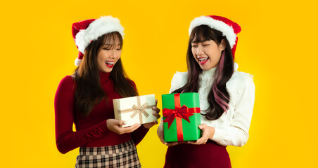 Young asian pretty woman in red and white color clothes wearing santa hat holding present boxes on yellow screen background. Merry Christmas and Happy New Year.