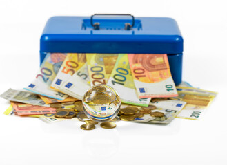 euro bills and coins lying on table and sticking out of blue cash box with reflection in glass ball