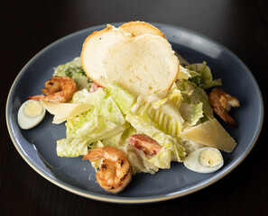 Italian caesar salad with grilled shrimp, croutons and parmesan cheese on black background.