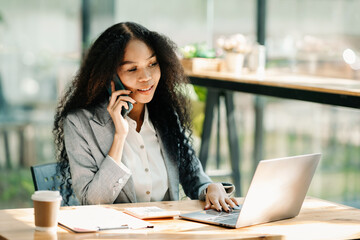 Business woman Talking on the phone and using a laptop with a smile while sitting at office..