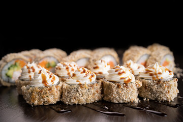 Set hot sushi rolls fried decorated cream cheese. Assortment of delicious tempura and baked sushi maki with salmon. Sushi volcano on black background