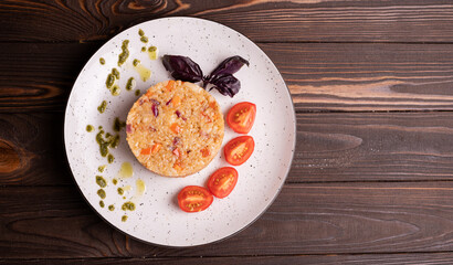 Fried rice with vegetables on a white plate with tomatoes and basil on a wooden background, top view