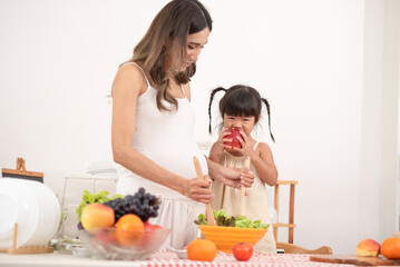 Mom with her two children eating fruits and vegetables. Mother with daughter having breakfast at home. Happy lifestyle family. Mother with her children in the kitchen cooking together.