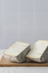 Two halves of round blue cheese wheel on wooden cutting board on light background, selective focus