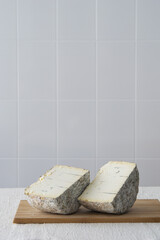 Two halves of round blue cheese wheel on wooden cutting board on light background, selective focus