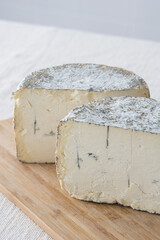 Two halves of round blue cheese wheel on wooden cutting board on light background, selective focus