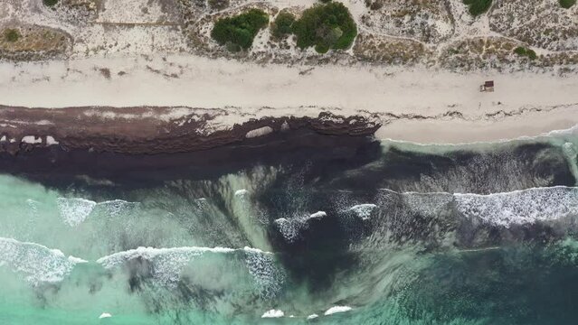 Aerial - drone view of the waves reaching a virgin white sand beach shore with no people