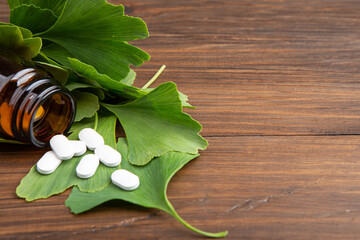 Bottle of pills and fresh ginkgo biloba leaves on wooden background. Traditional, herbal medicine and Homeopathy concept.