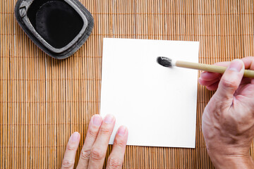 Abstract man hand white paper with bamboo calligraphy brush and inkstone on bamboo mat. picture for...