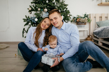 Happy smiling family at studio on background of the Christmas tree with gift