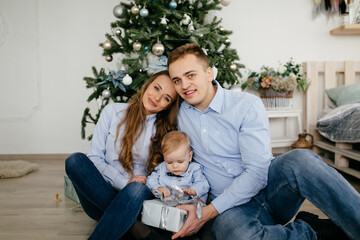 Happy smiling family at studio on background of the Christmas tree with gift